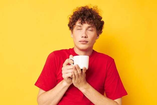 Chico con pelo rizado rojo posando con una taza blanca y en manos de una bebida aislado fondo inalterado