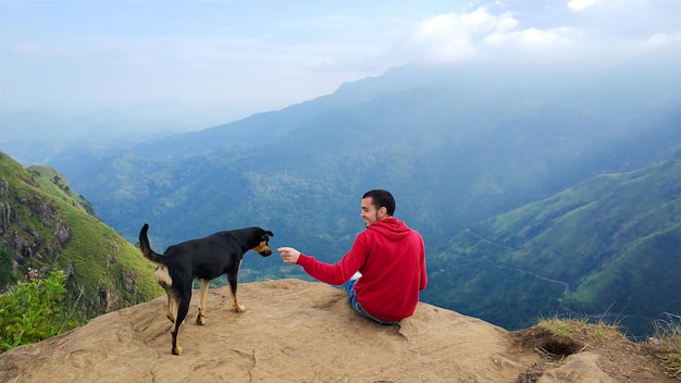 Un chico con un perro disfrutando del paisaje de montaña al borde de un acantilado