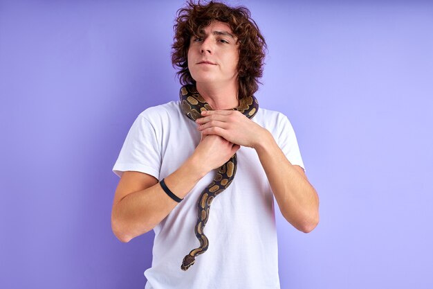 Chico de pie con serpiente en el cuello, es valiente, no tiene fobia. fondo morado aislado