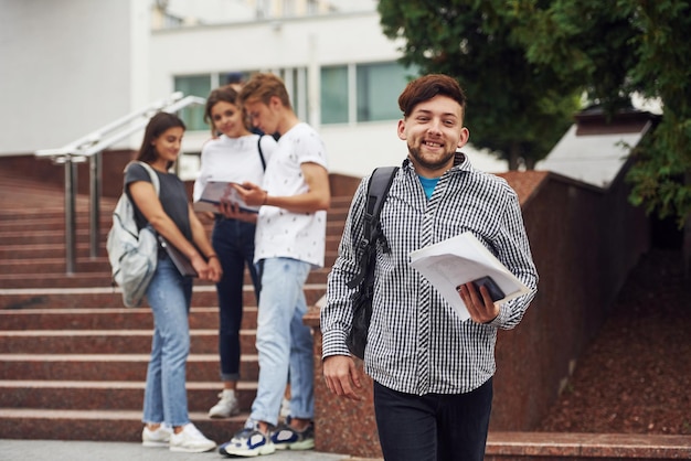 Chico positivo. Grupo de jóvenes estudiantes con ropa informal cerca de la universidad durante el día.