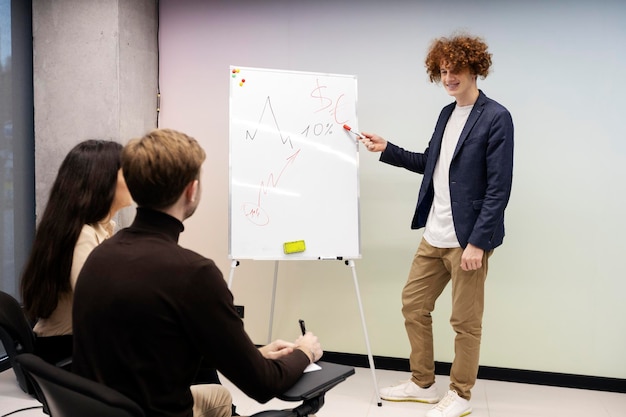 Chico positivo sonriente apuntando al gráfico dibujado en el rotafolio El joven entrenador da una conferencia a los estudiantes