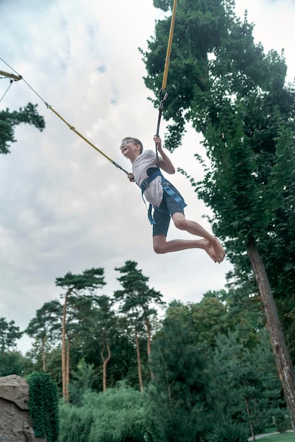 Chico puenting en trampolín Adolescente en un parque de diversiones se divierte Marco vertical