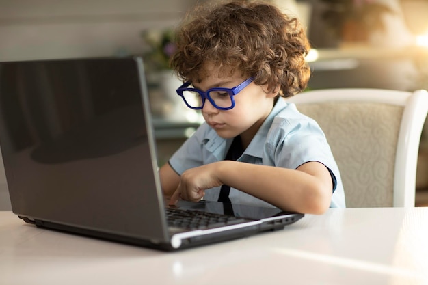 El chico rizado con anteojos se dedica a un libro de computadora portátil mira cuidadosamente el monitor