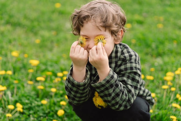 Foto chico rizado recoge y huele flores de diente de león