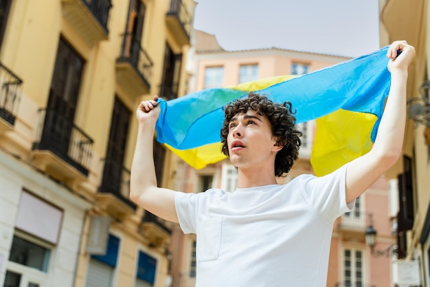 Chico rizado sosteniendo la bandera ucraniana en la calle y mirando hacia otro lado con esperanza