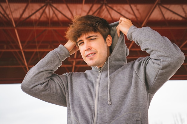 Chico en ropa deportiva sonriendo y poniéndose su sudadera con capucha y mirando a la cámara Actitud