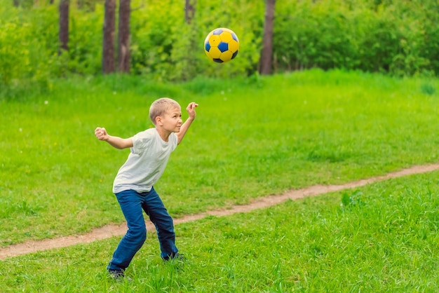 Chico rubio con una camiseta blanca jugando con una pelota de fútbol en el parque