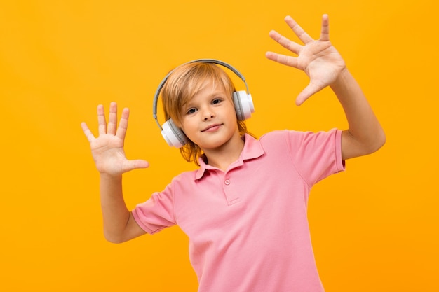 Chico rubio europeo con una camiseta rosa sale a la música con auriculares blancos sobre naranja