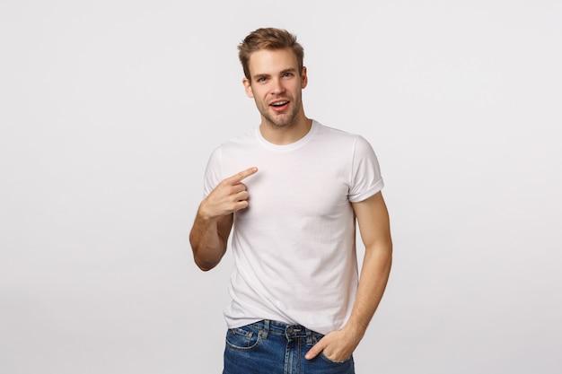 Foto chico rubio guapo con ojos azules y camiseta blanca apuntando a sí mismo