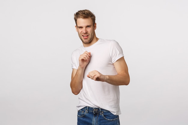 Chico rubio guapo con ojos azules y camiseta blanca haciendo muecas y entrecerrando los ojos por la aversión