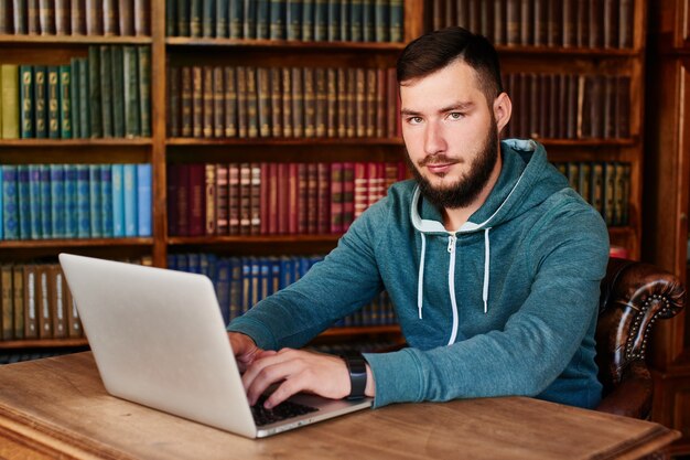 El chico sentado en la mesa con el portátil en el fondo de los libros