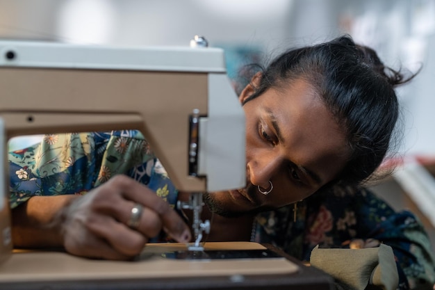 Chico serio de etnia india poniendo hilo en el ojo de la aguja de la máquina de coser