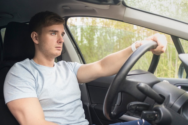 Chico serio guapo, conductor, joven concentrado se centró en el hombre de la carretera conduciendo un automóvil, sosteniendo el volante del automóvil con las manos. Niño dentro del coche sentado no abrochado por el cinturón de seguridad. Desabrochado