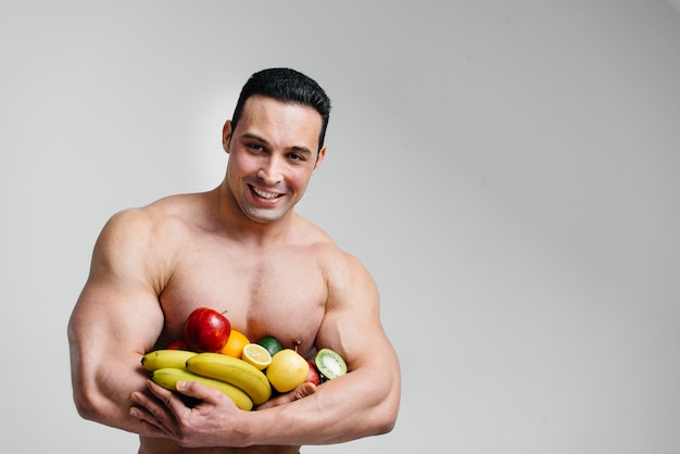 Chico sexy deportivo posando sobre un fondo blanco con frutas brillantes. Dieta. Dieta saludable