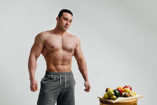 Chico sexy vegano con un torso desnudo posando en el estudio junto a la fruta. Dieta. Dieta saludable.