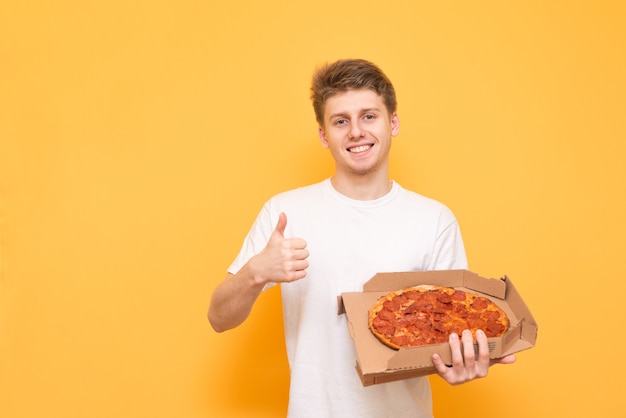 Chico sonriente con una camiseta blanca está de pie con una caja de pizza en sus manos