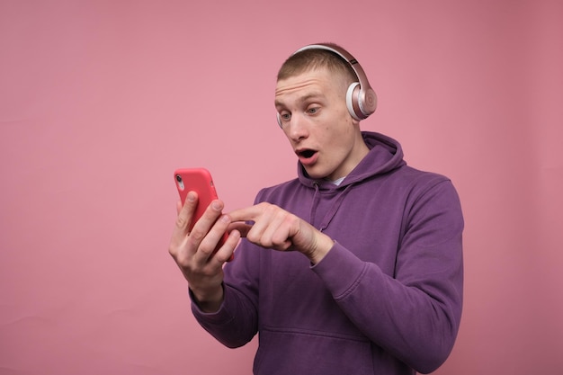 chico sorprendido usando auriculares y apuntando a su teléfono