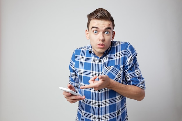 chico sorprendido vestido con una camisa a cuadros y jeans mantiene el teléfono móvil en la mano