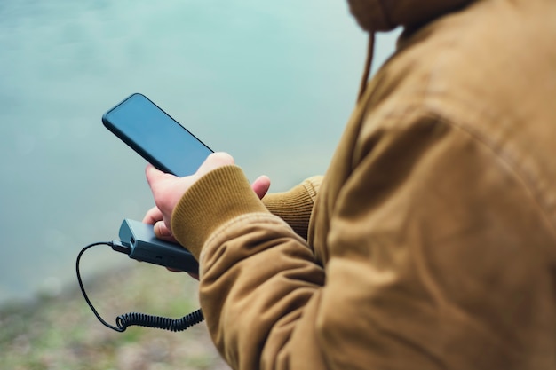 El chico sostiene un cargador portátil con un teléfono inteligente en la mano.