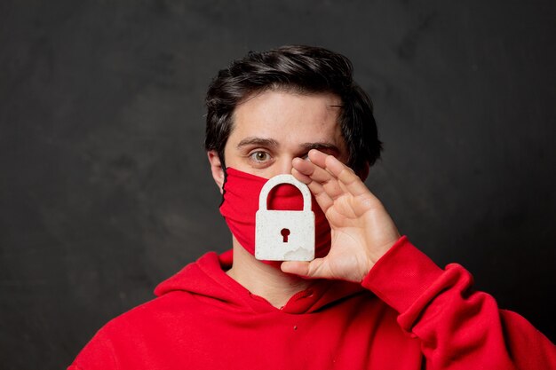 Chico en sudadera roja y mascarilla mantenga el candado en la pared oscura