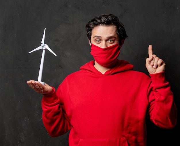 Chico en sudadera roja y mascarilla sostiene pequeño generador de viento en la pared oscura