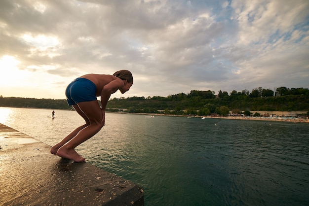 Chico se sumerge en el mar desde un muelle Día caluroso de verano