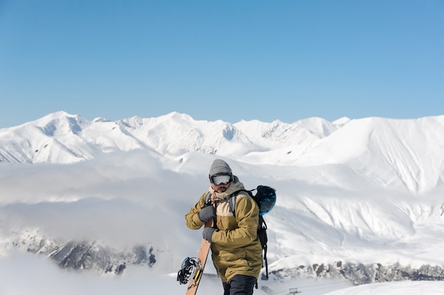 Chico con una tabla de snowboard de madera en sus manos se encuentra en las montañas