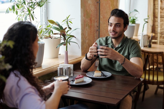 Chico con taza de café y su novia sentados junto a la mesa en el café