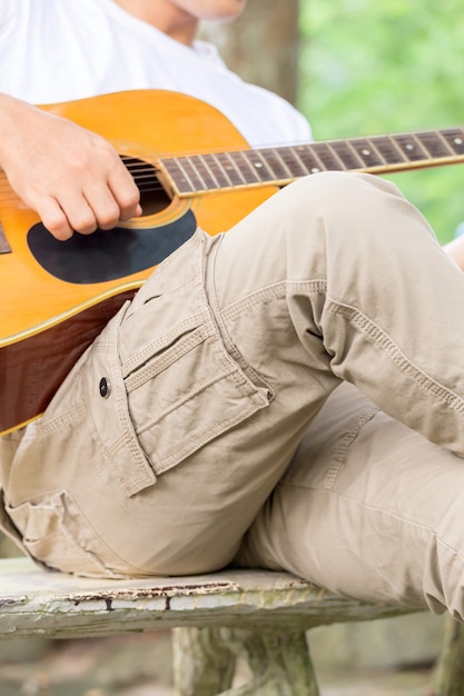 El chico tocando la guitarra, al aire libre, pantalones de carga.