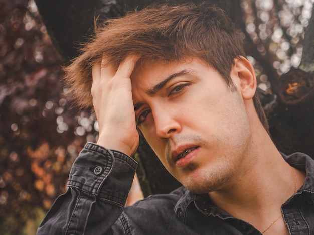 Chico tocando su cabello mirando a la cámara en un parque