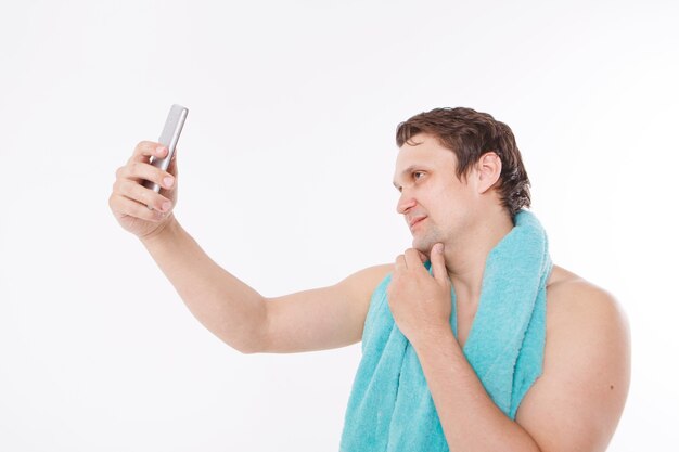 El chico se toma una selfie después de los procedimientos matutinos. Un hombre mira la cámara del teléfono. Rostro bien afeitado. Toalla azul alrededor de su cuello. Hombre y tecnologías modernas. la conversación a través del enlace de video