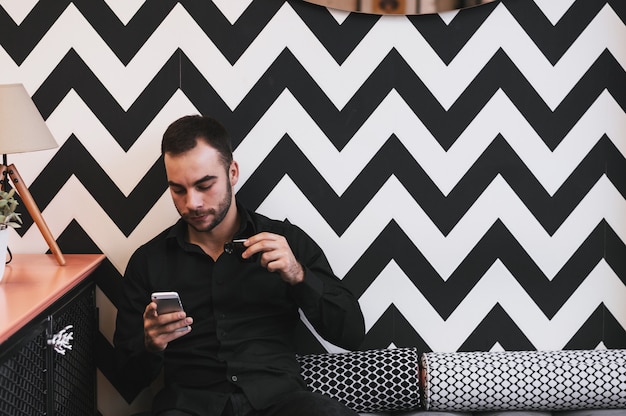 Chico tomando el primer café de la mañana mientras revisa los correos electrónicos en el móvil