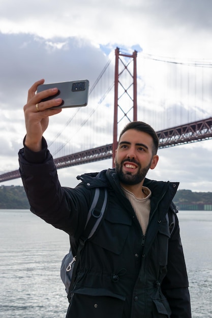 Chico tomando un selfie con su teléfono móvil en el Puente 25 de abril Lisboa Portugal