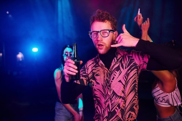 Chico en vasos bebe cerveza Los jóvenes se divierten en el club nocturno con luces láser de colores