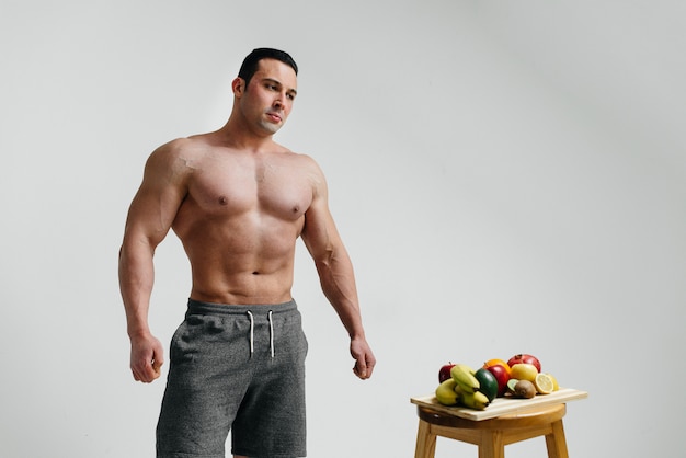Chico vegano sexy con un torso desnudo posando en el estudio junto a la fruta. Dieta. Dieta saludable