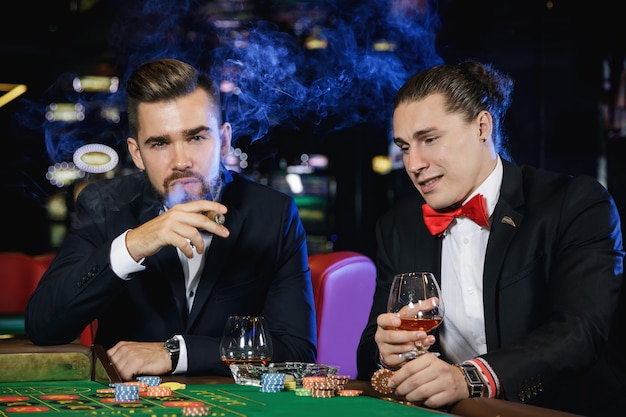 Chicos guapos bebiendo coñac y jugando a la ruleta en el casino