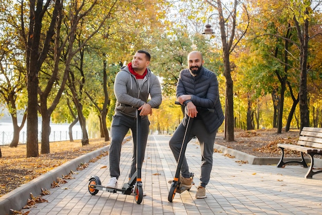 Chicos jóvenes viajan por el parque en un scooter eléctrico en un cálido día de otoño. Caminar en el parque.