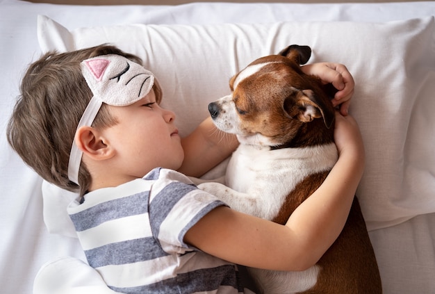 Chihuahua Hund und Vorschulkind schlafen in Kitty Schlafmaske und liegen im Bett. Hund umarmen.