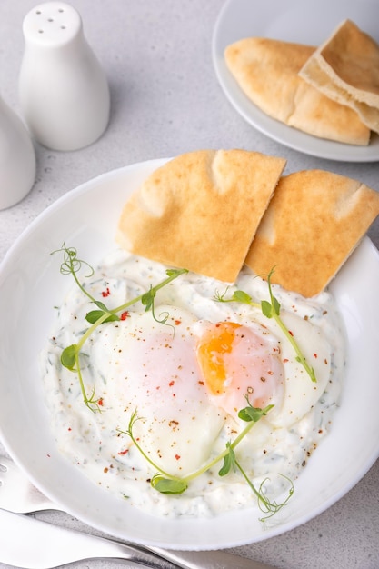 Chilbir de huevos turcos con brotes de guisantes de mantequilla fragantes de yogur pan plano y té Desayuno turco tradicional con huevos escalfados con yema líquida Primer plano de enfoque selectivo