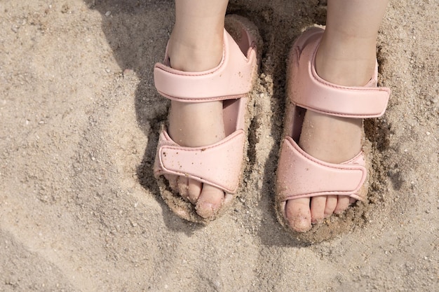 Children39s Beine in rosa Sandalen auf dem Sand Sommersonne Strandurlaub Platz für Text