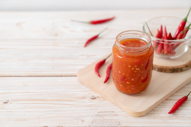 Chile o salsa de ají en botella y jarra sobre mesa de madera