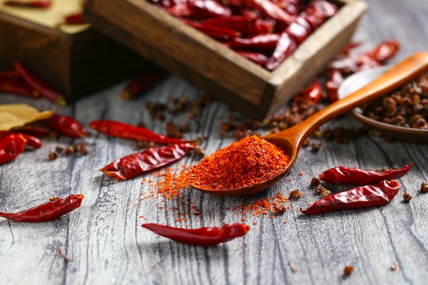 Chile en polvo en una cuchara de madera y pimiento seco en la mesa de madera gris