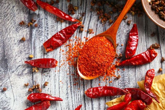 Chile en polvo en una cuchara de madera y pimiento seco en la mesa de madera gris