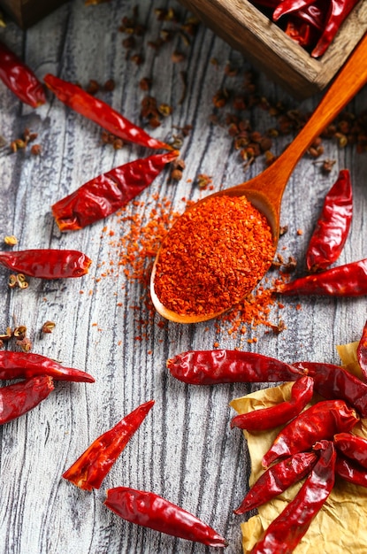 Foto chile en polvo en una cuchara de madera y pimiento seco en la mesa de madera gris