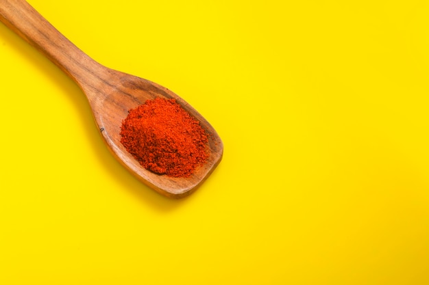 Chile en polvo en una cuchara de madera con rojo seco frío sobre superficie amarilla