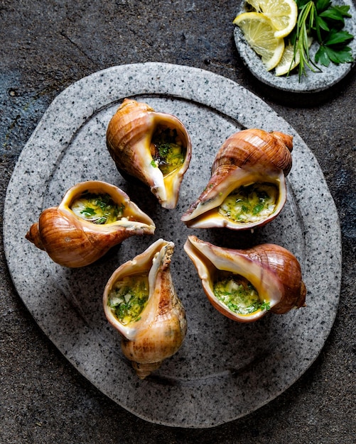 Chilenische Riesenschnecken mit Butterknoblauch und Kräutern auf grauer Steinplatte, Schnecken aus dem Pazifischen Ozean