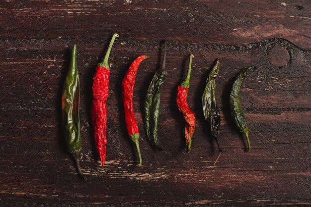 Foto chiles rojos y verdes picantes secos sobre madera con textura marrón.