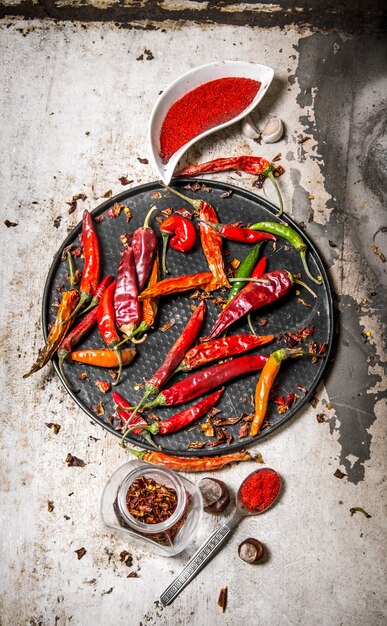 Chiles secos en bandeja con pimiento rojo triturado en tazas, con hierbas en mesa rústica. Vista superior