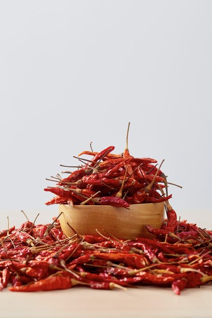 Chiles secos en un recipiente de madera colocado sobre una mesa de madera y una pared blanca para copiar el espacio para el texto