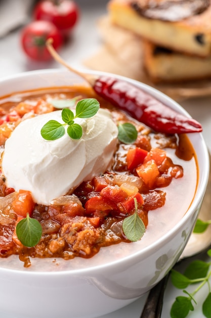 Chili com Carne. Receita tradicional. Grande porção de guisado com feijão, pimenta, especiarias e ervas frescas. Uma grande porção é servida em uma tigela com creme de leite fresco.